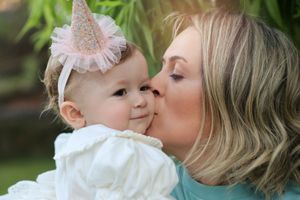 A tender moment captured between parent and baby wearing a sparkly party hat against a soft green background.