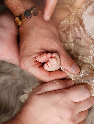 Close-up of tiny baby hand being held by adult hands with beaded bracelet.