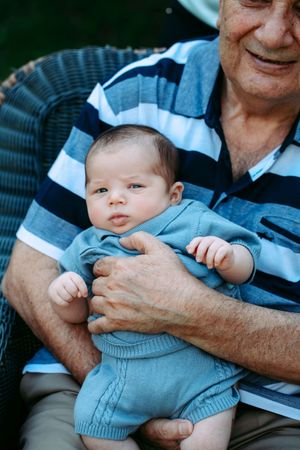 Baby in blue outfit being held on lap outdoors.