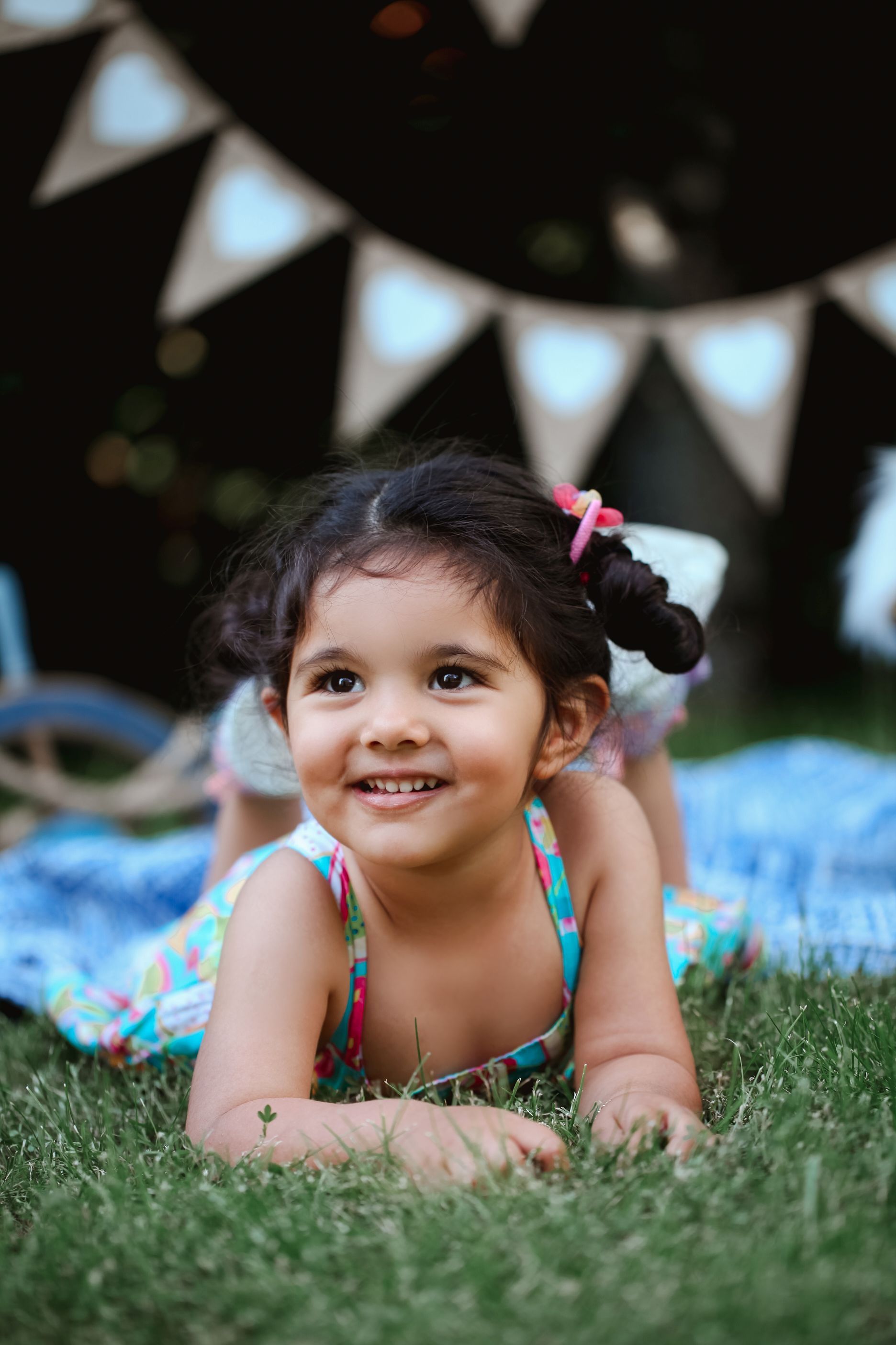 Child lying on grass under party bunting decorations during summer celebration.