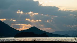 Dramatic sunset sky with clouds casting golden light over mountains and water.