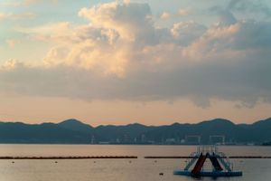 Panoramic view of a calm ocean bay with mountains and clouds at sunset.