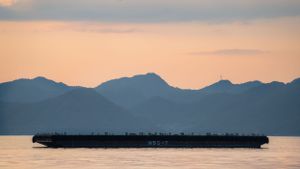 Silhouetted mountain range against a pink and purple sunset sky over water.