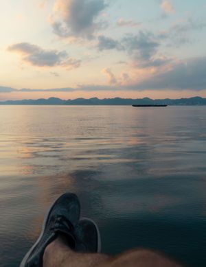 Peaceful ocean view at sunset with mountains in the distance and feet in sandals visible.