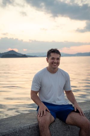 Person relaxing on a concrete barrier by the ocean during golden hour sunset.