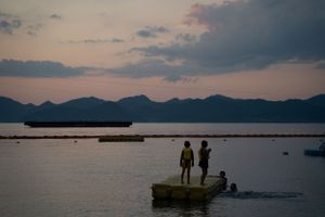 Silhouettes of people on a dock at sunset with mountains in the background.