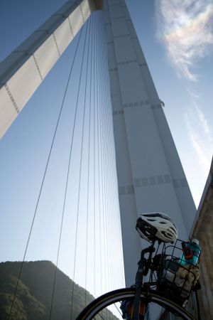 Bicycle silhouette against towering white bridge support and cables.