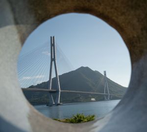 Cable-stayed bridge spanning across mountains viewed through circular frame.