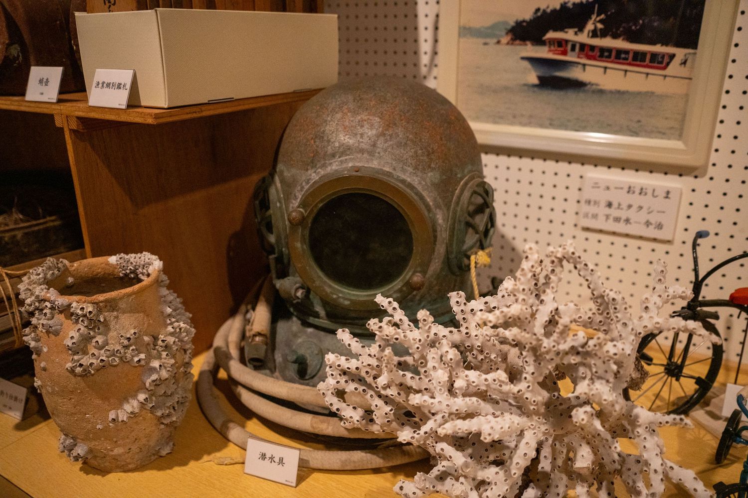 Vintage diving helmet displayed with coral and nautical artifacts in museum setting.
