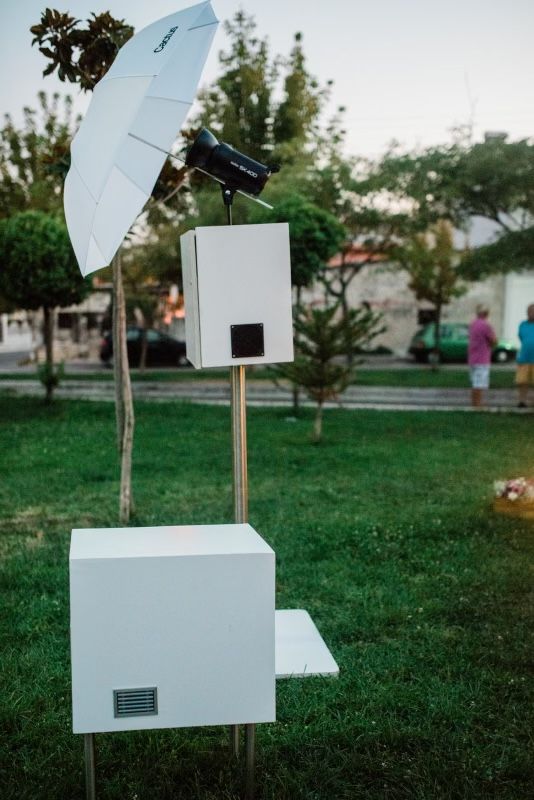 Portable open-air photo booth set up on grass for an event with a white lighting umbrella.
