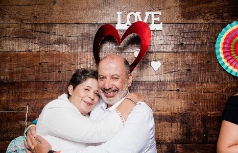 Two guests posing for a fun photo booth picture in front of a rustic wooden backdrop with "LOVE" signs and party props.