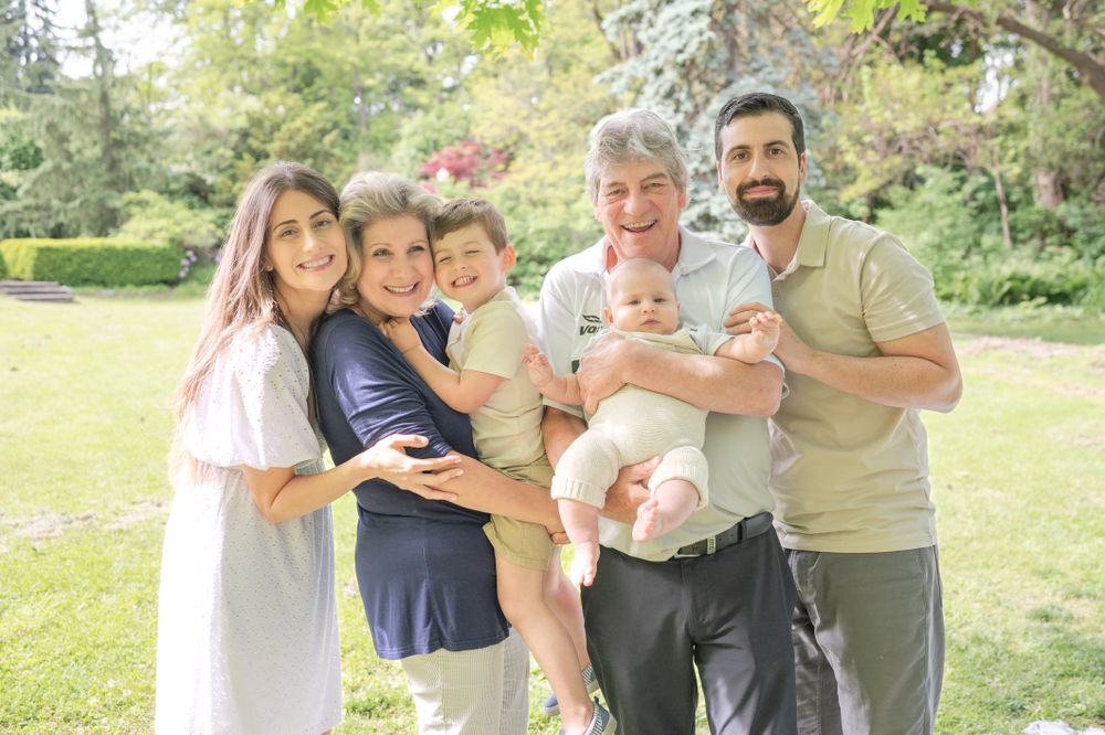 A heartwarming family portrait of adults and children gathered outdoors in a sunny garden setting.