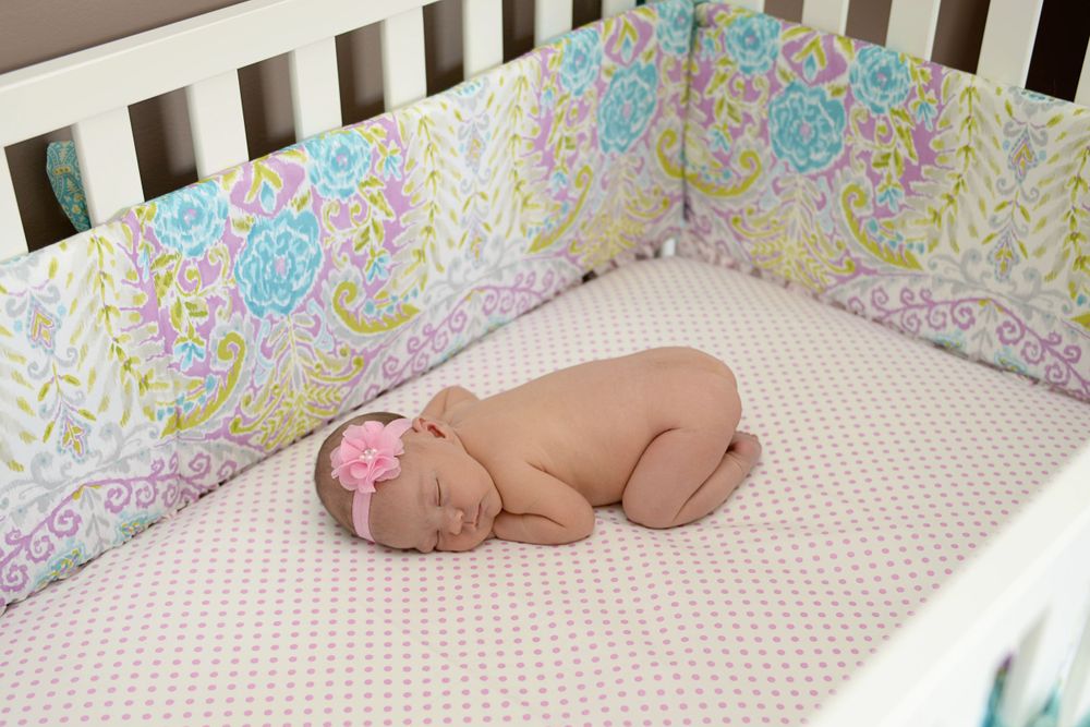 Newborn baby sleeping peacefully in a polka dot crib with floral patterned bedding.