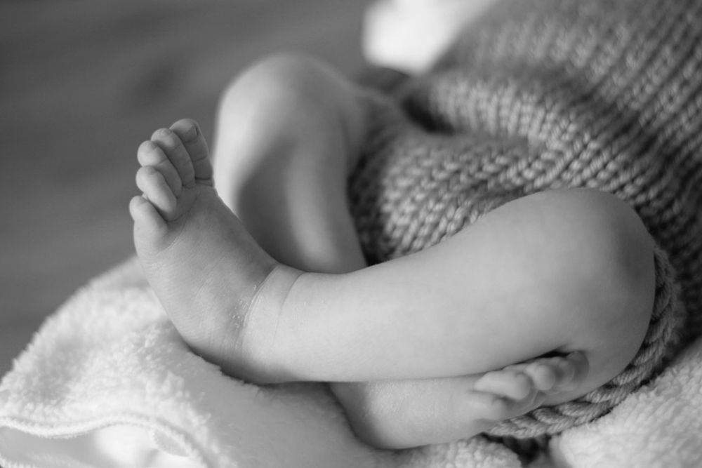 Close-up black and white photo showing delicate details of baby's knitted clothing and soft textures.