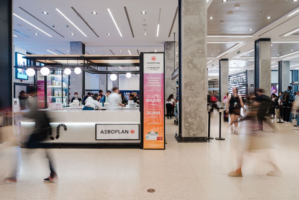 Busy shopping mall interior with motion-blurred customers walking past retail counters and displays.