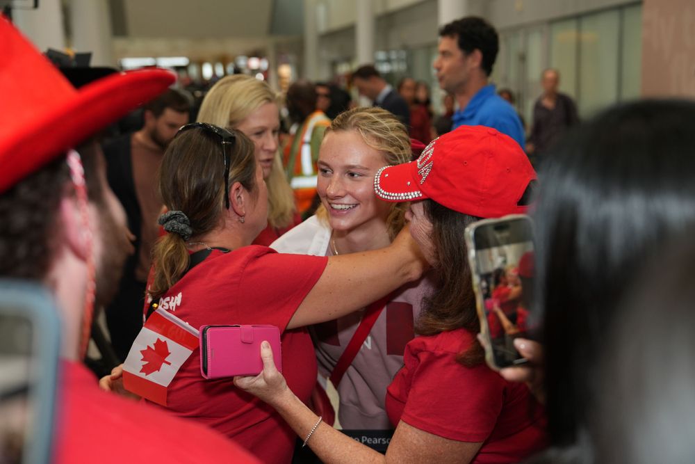 Group celebration with people wearing red and white Canadian attire embracing in crowd.