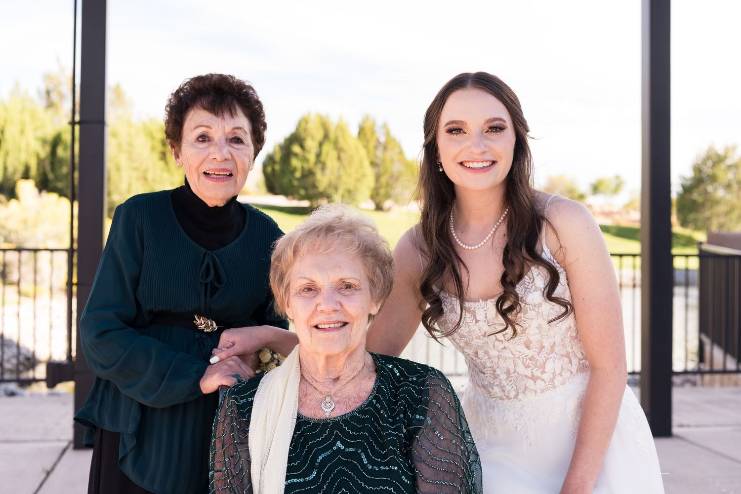 Three generations pose together outdoors at a formal event wearing elegant dresses.