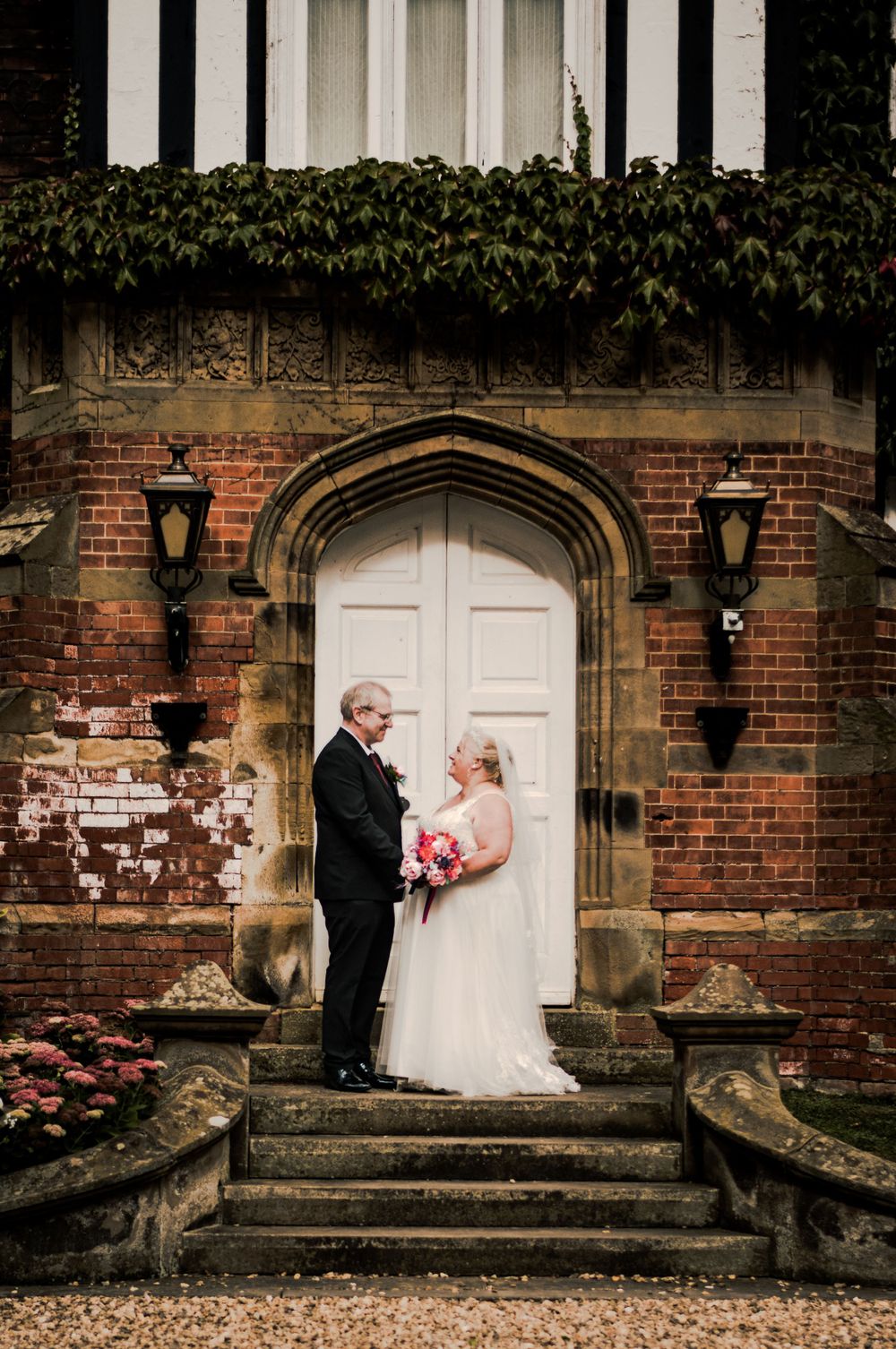 A couple standing in a romantic brick archway entrance with climbing vines and lanterns during their wedding day.