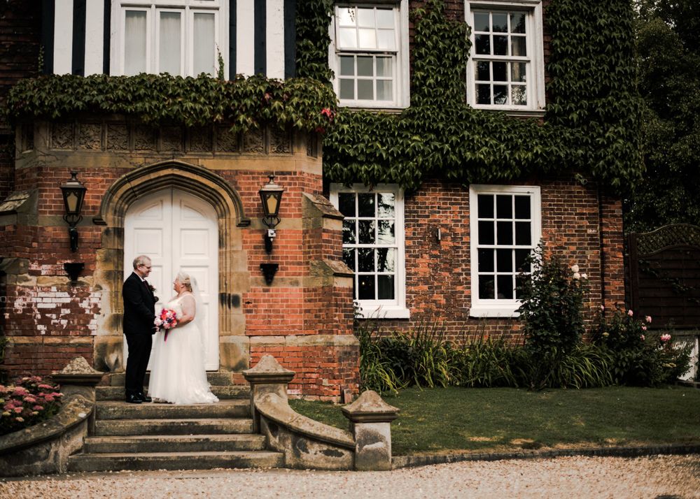 Couple poses for wedding photos at entrance of ivy-covered brick mansion.