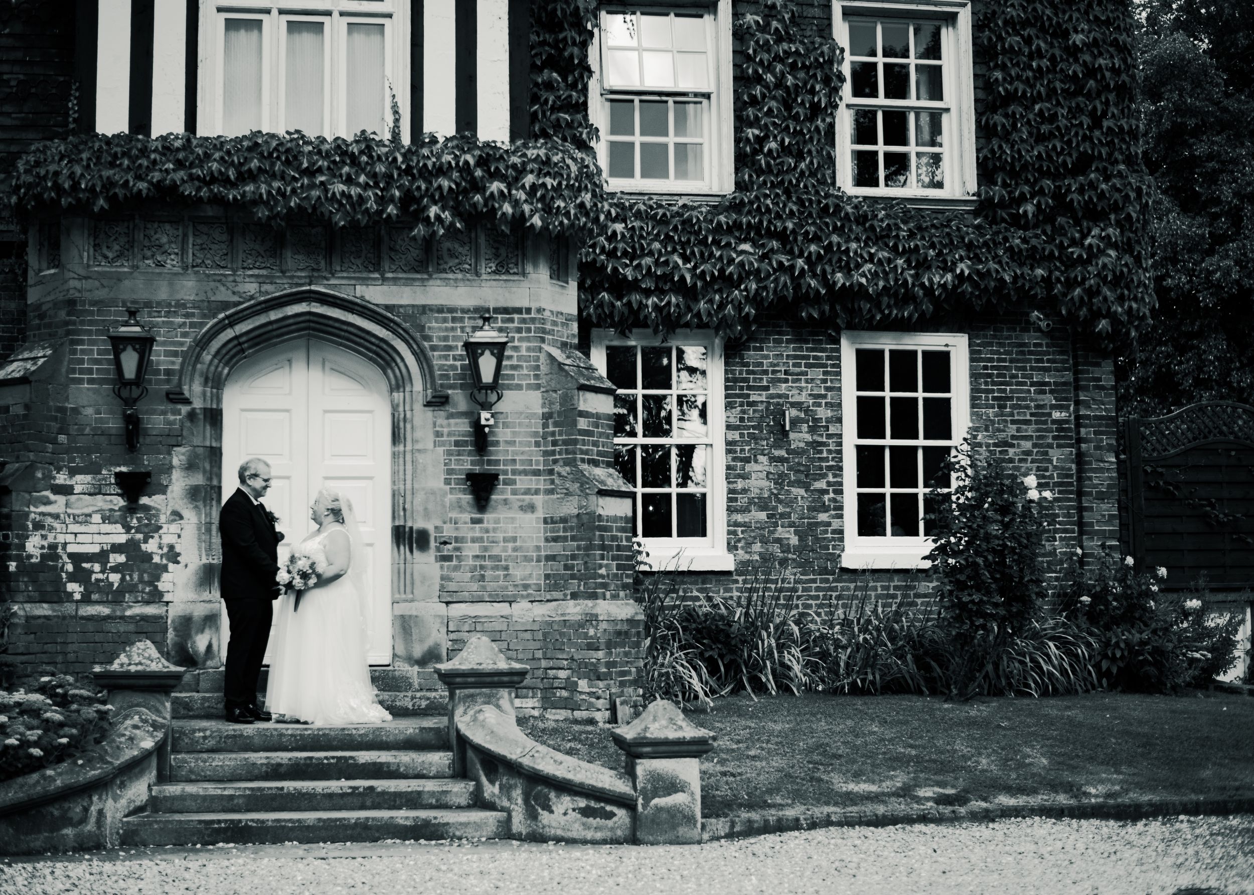 Black and white wedding portrait in front of historic brick building with arched doorway.