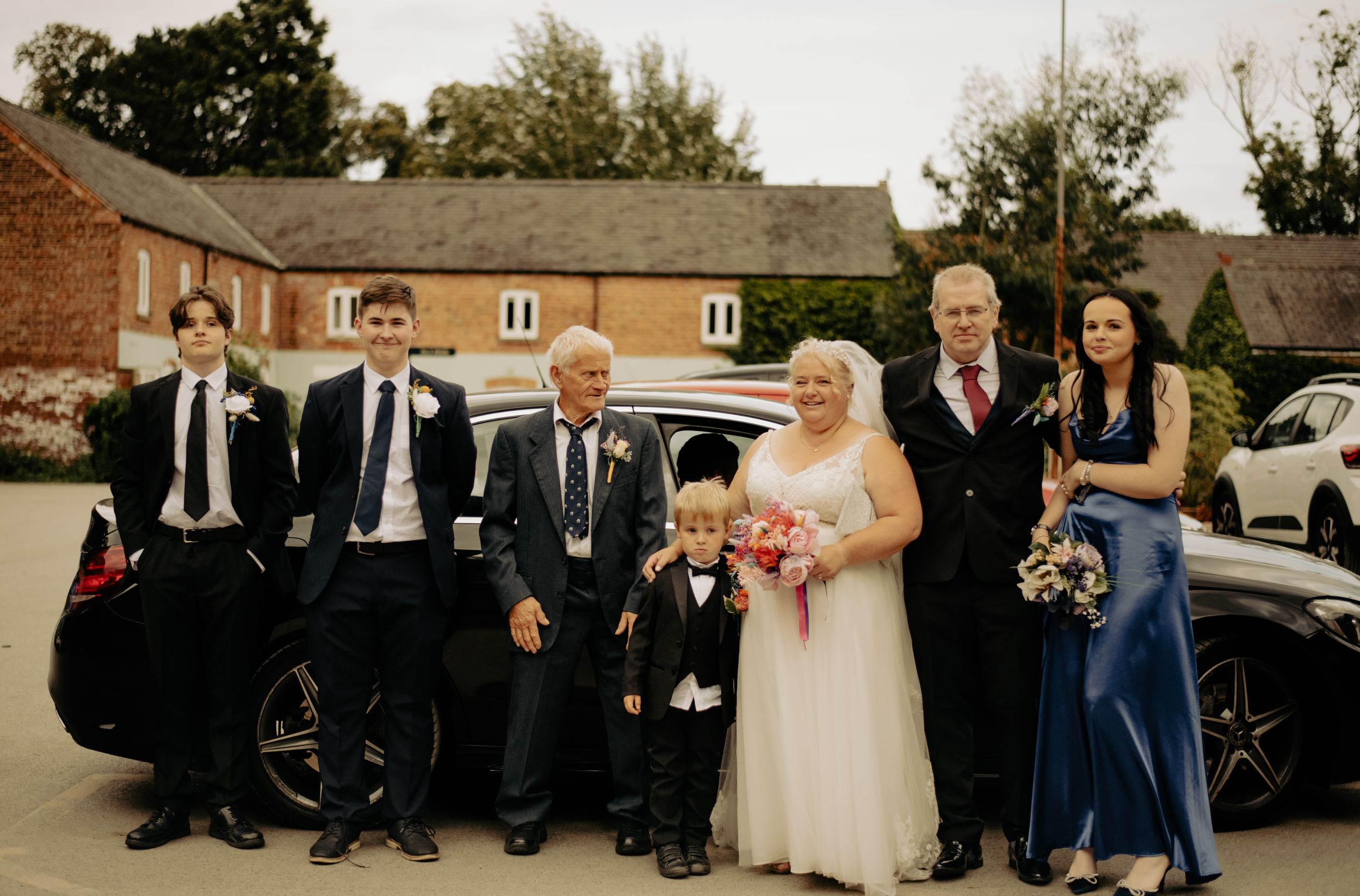 Wedding party poses together in formal attire outside brick building.