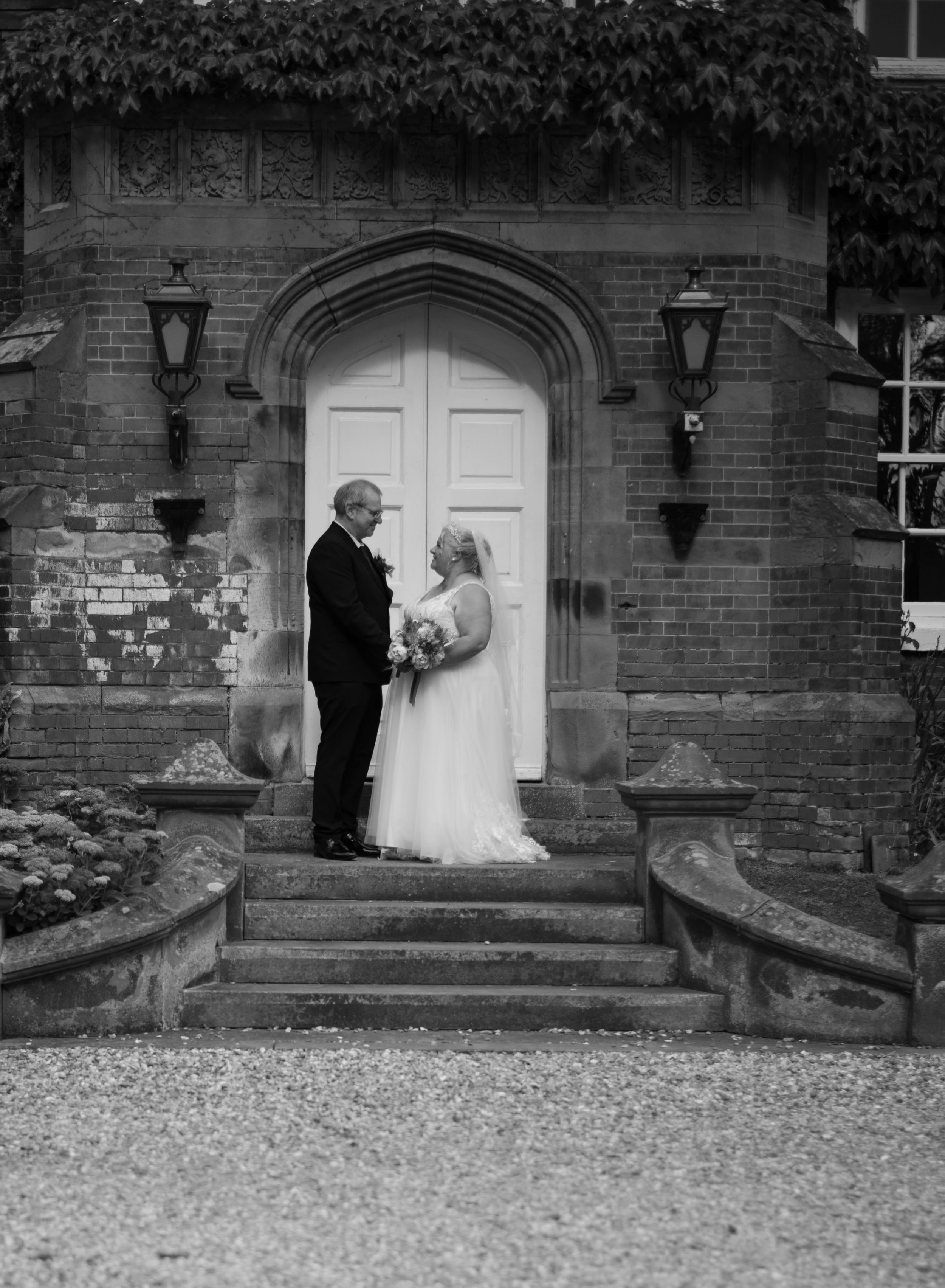 Couple poses in formal attire on stone steps in front of an ivy-covered brick entrance with white door.