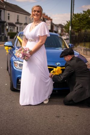A wedding scene with a white dress and blue car on a residential street.
