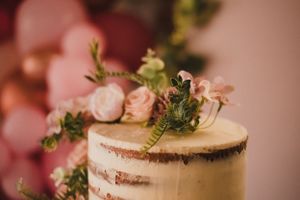 Close-up detail of wedding cake featuring delicate pink floral decorations and rustic styling.