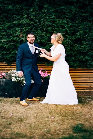 A playful wedding photo with a couple dancing in front of greenery and a wooden fence.