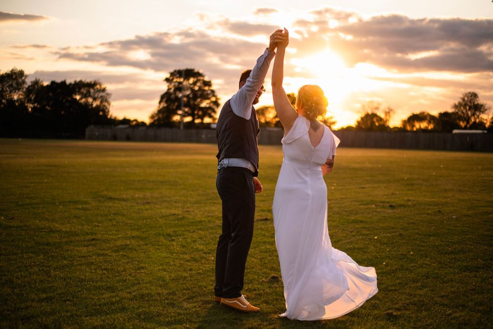 A couple dancing in a sunset-lit field during their wedding celebration.