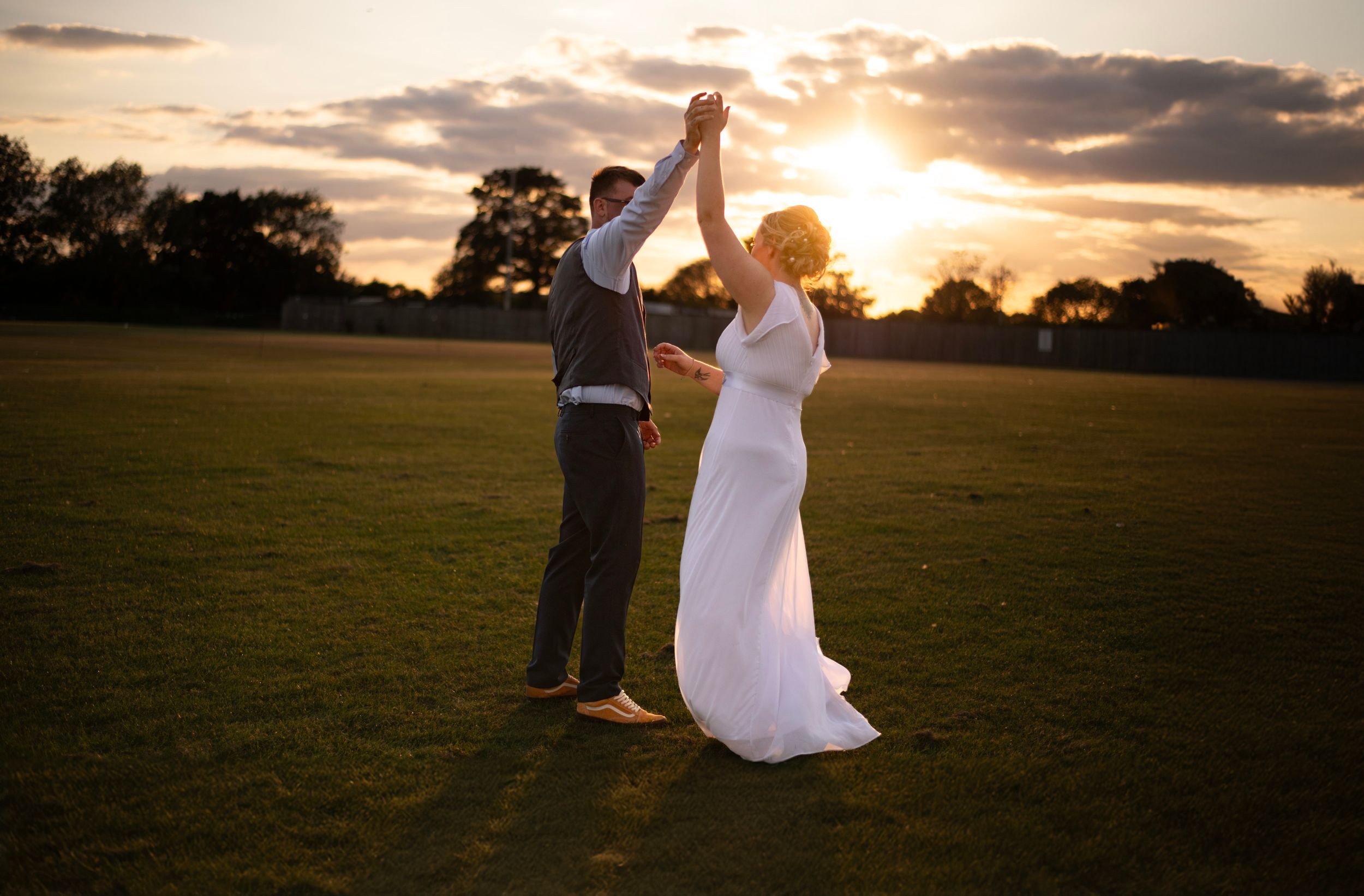 A romantic dance pose silhouetted against a golden sunset on an open field.