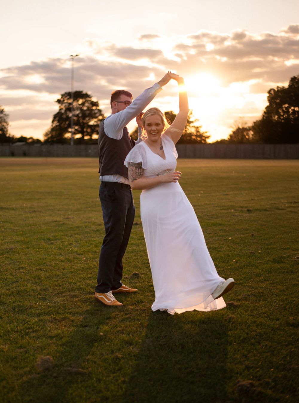 A couple dancing and twirling together at sunset in an open field.