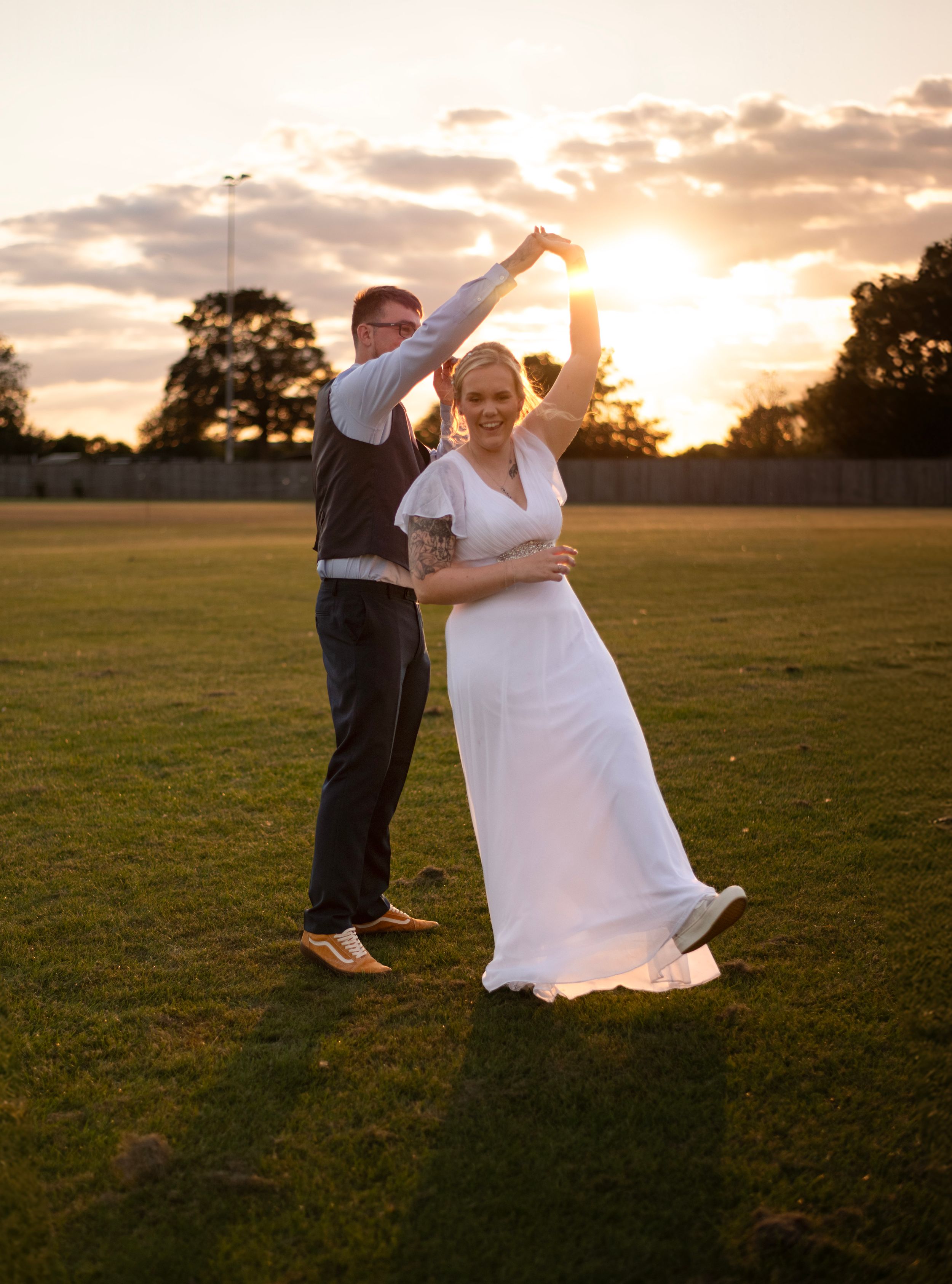 A couple dancing and twirling together at sunset in an open field.