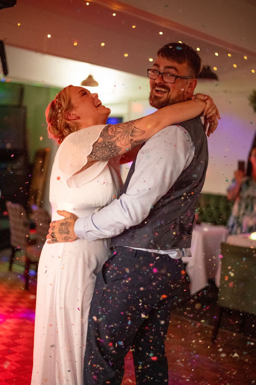 A couple sharing their first dance amid colorful lights and confetti at their wedding reception.