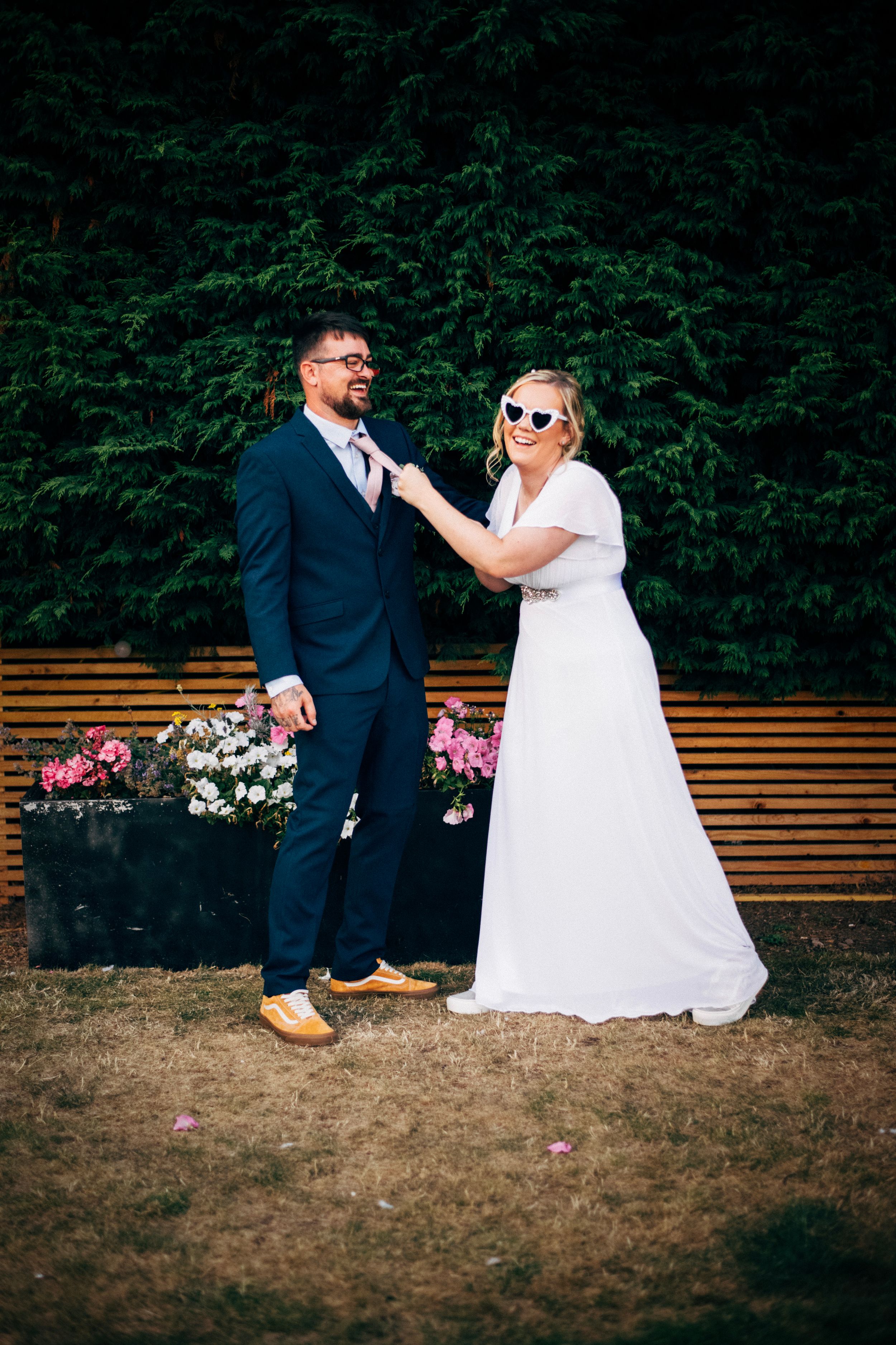 A playful wedding portrait taken against a backdrop of evergreen trees and wooden fencing.