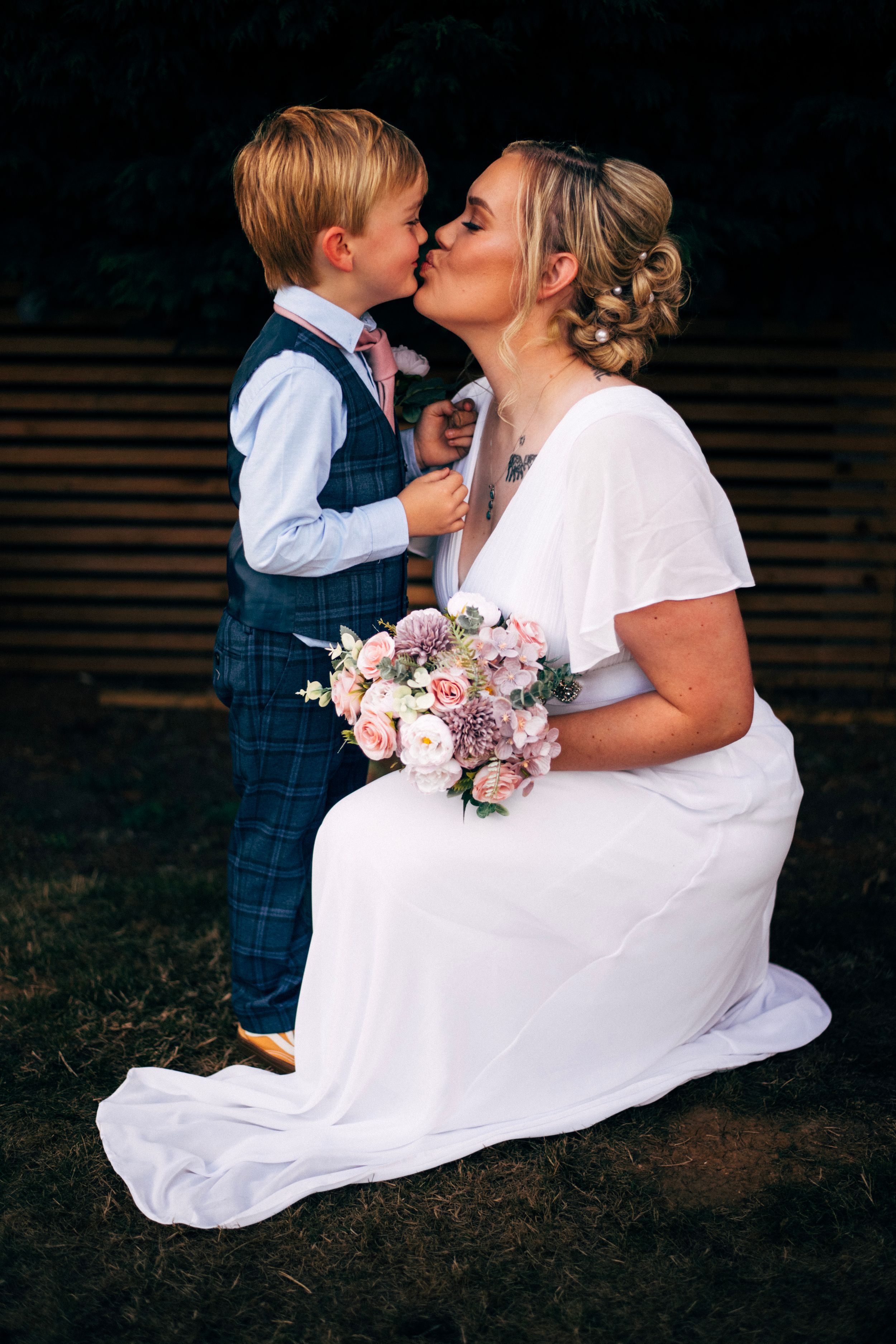 Sweet moment between bride and young attendant with pink floral bouquet in outdoor garden setting.