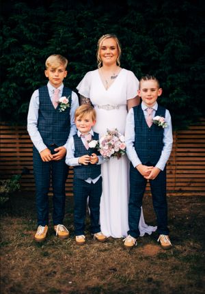 Wedding party portrait showing bride in white dress with young attendants in matching navy vests.