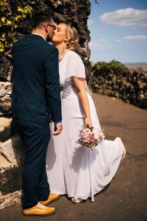 Intimate wedding portrait of couple kissing against stone wall with bride holding pink bouquet.