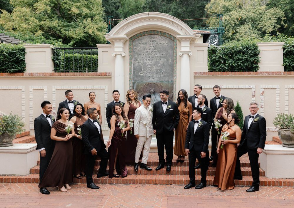 Wedding party in formal attire posed together against a stone wall backdrop.