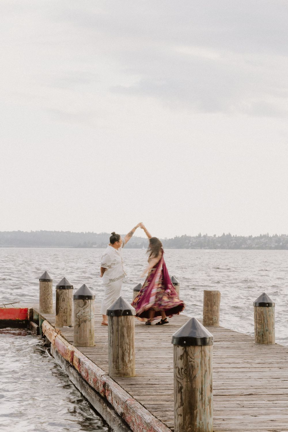 A couple dancing on a wooden pier over a lake with ornate posts and cloudy skies in the background.