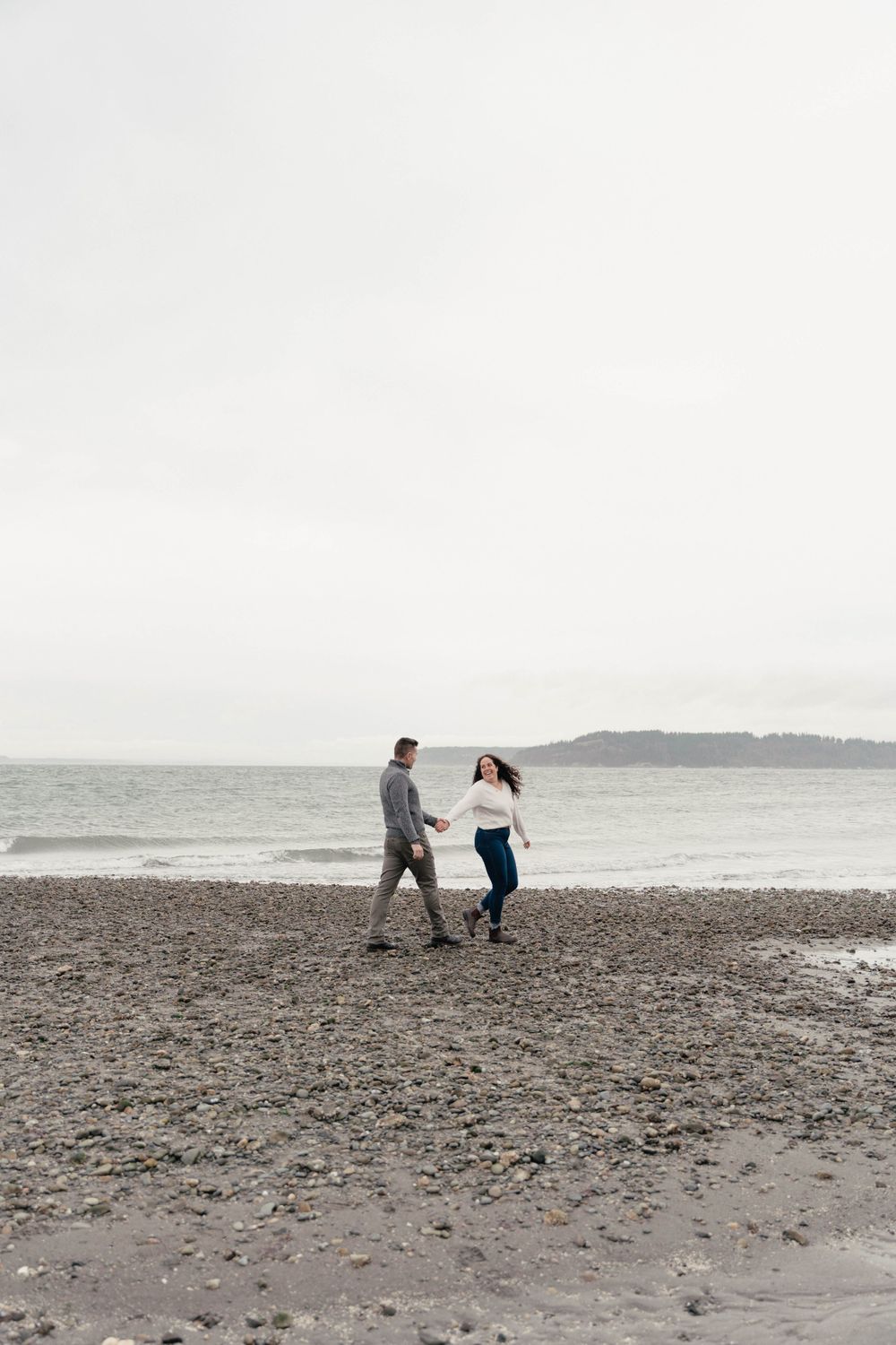 A couple walking together on a rocky beach with overcast skies.