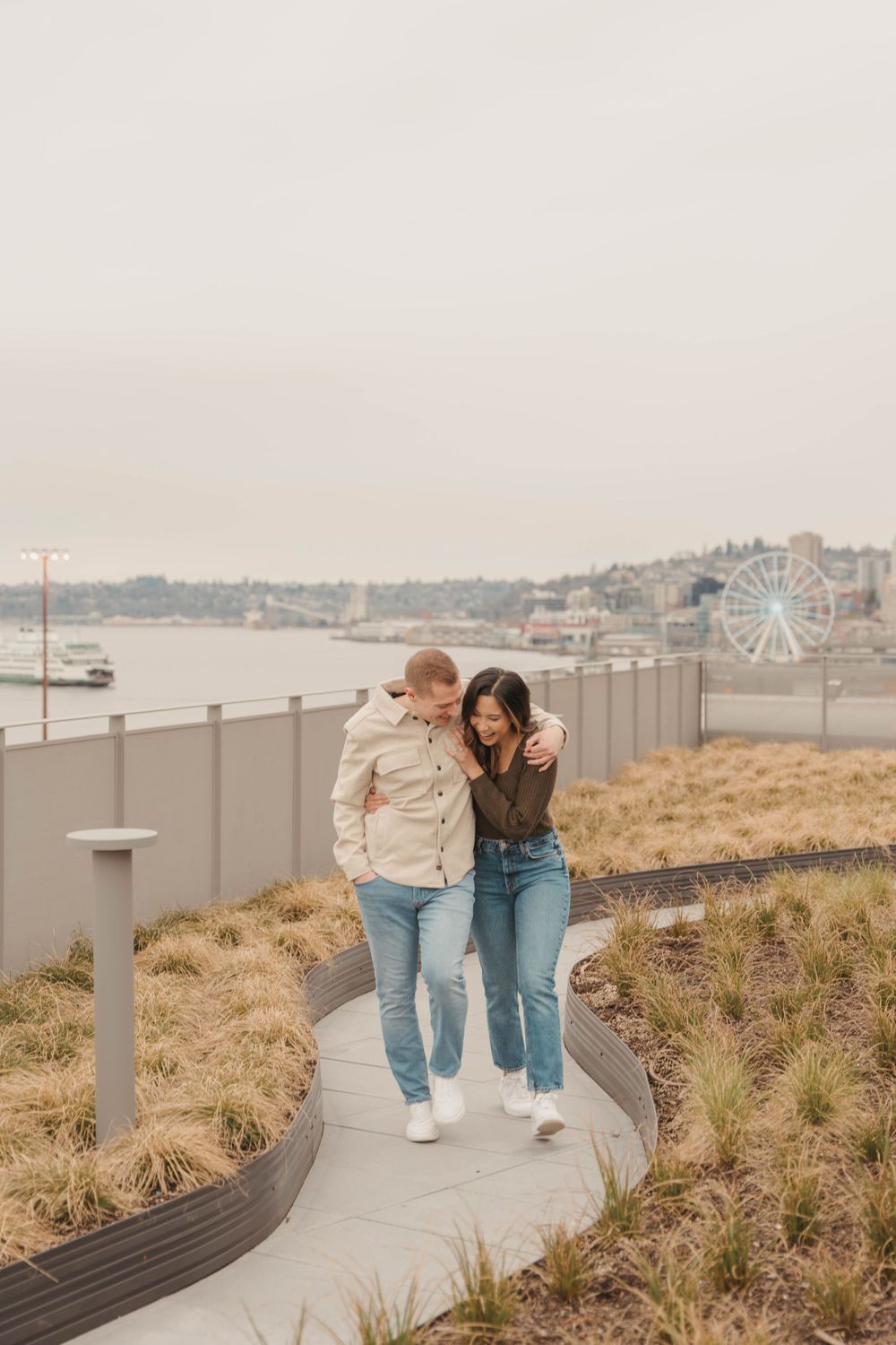 Two people walking together on a curved path with a waterfront and Ferris wheel in the background.