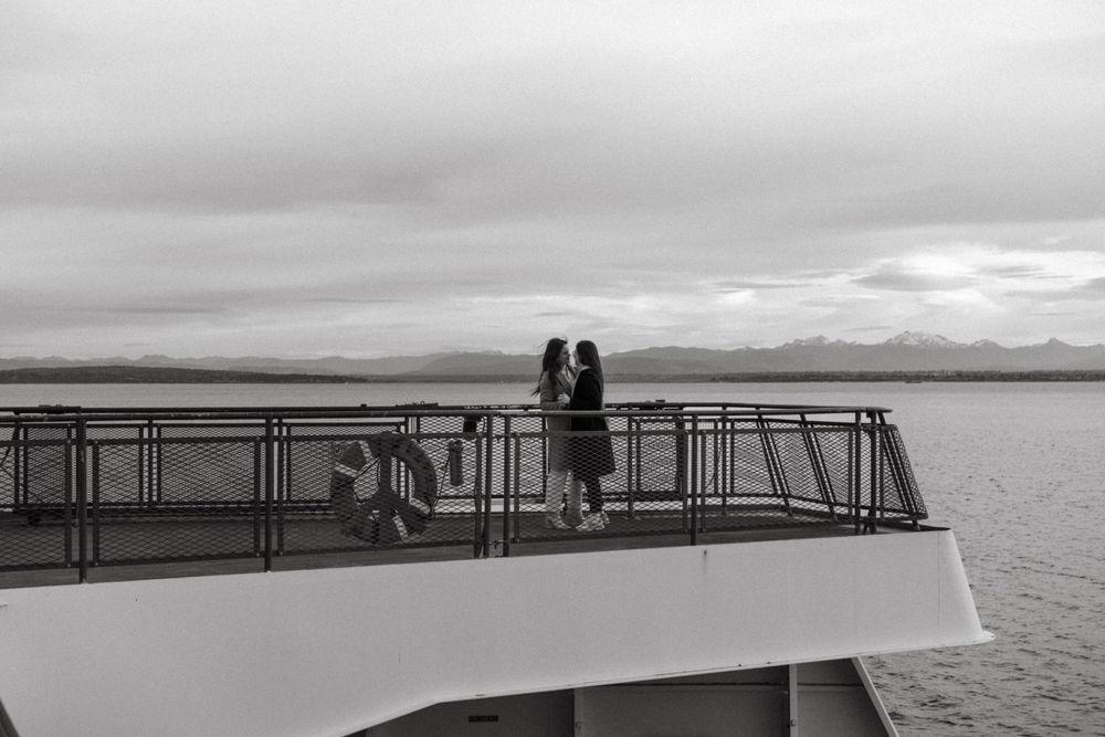 Two silhouettes standing together on a boat deck overlooking a misty waterfront landscape.