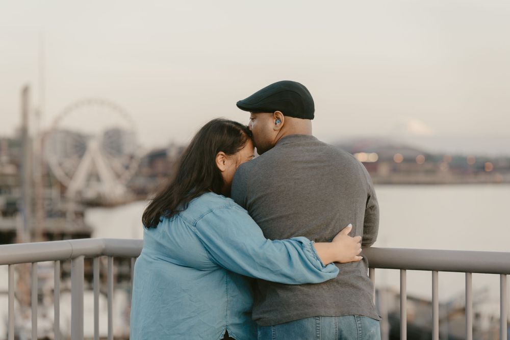 A couple embracing while looking out over the water with a ferris wheel visible in the distance.