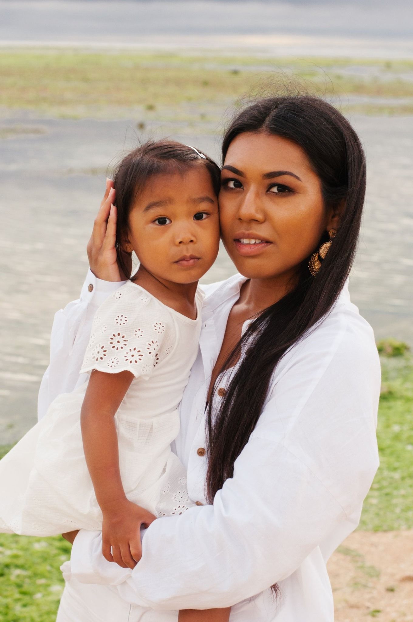 Tender moment between parent and child wearing white outfits outdoors.