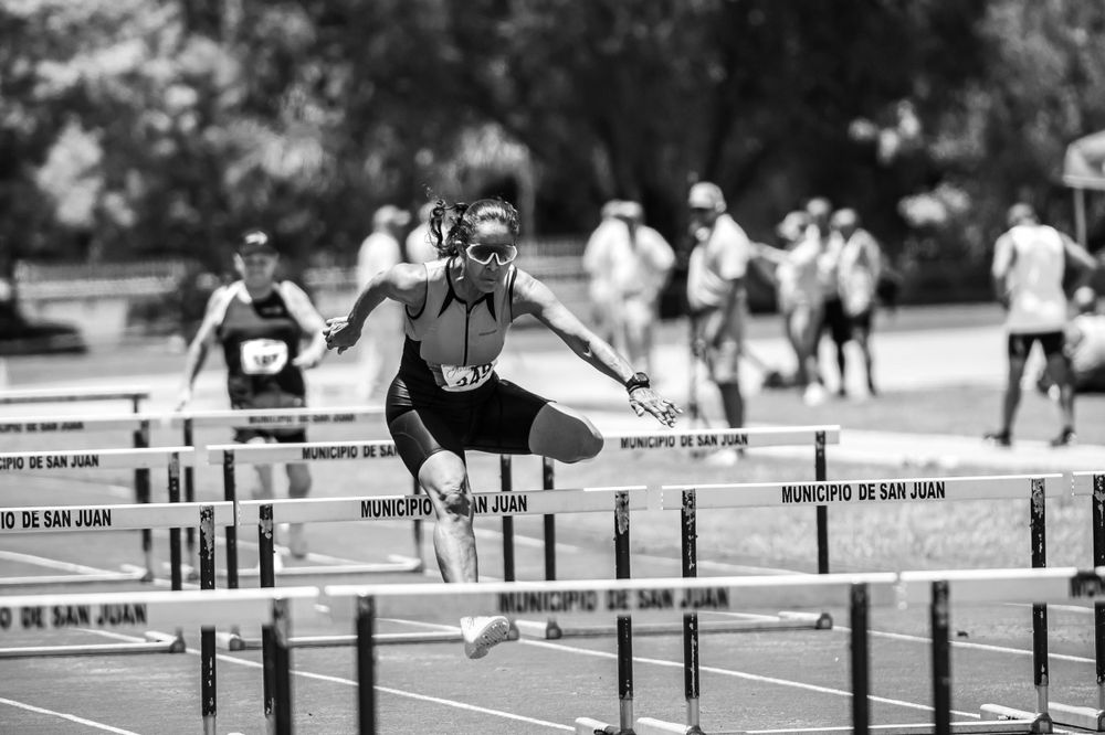 Athletes clearing hurdles during a track competition on an outdoor field.