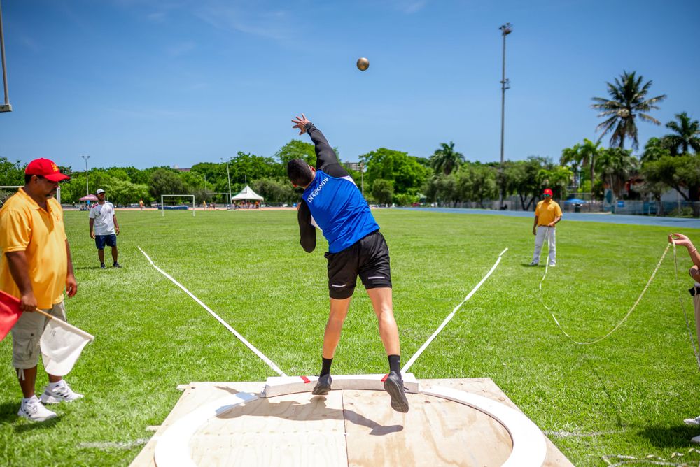 Athlete performing shot put throw at an outdoor track and field competition.