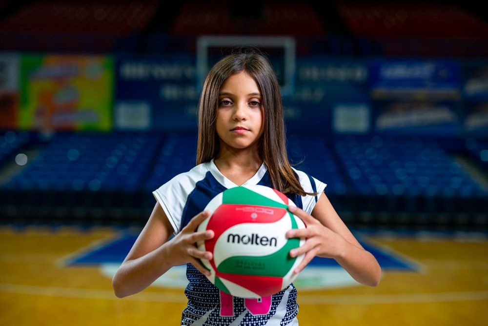 Player holding white and green volleyball in indoor sports arena.