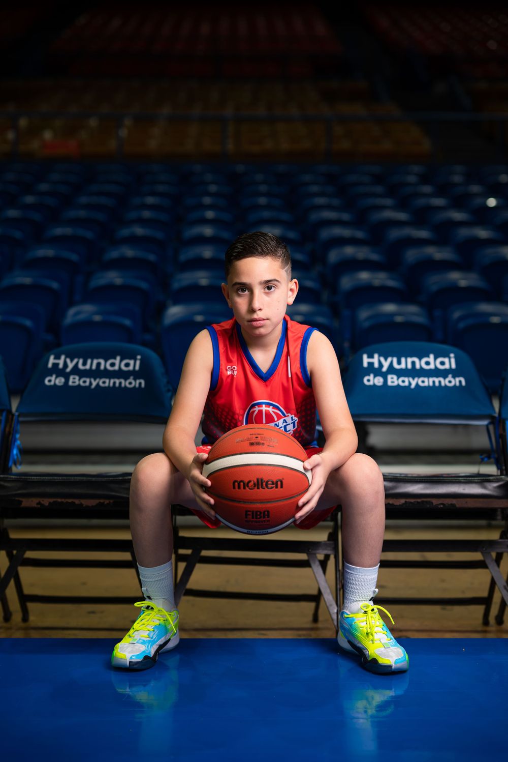 Young athlete sitting with basketball in empty stadium seating area.