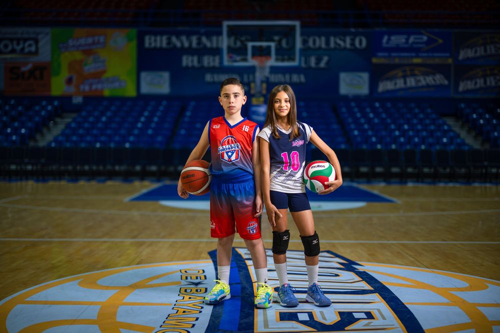 Two basketball players posing with their balls on indoor court.